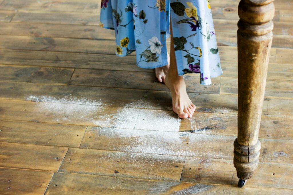 Female feet on the wooden floor of the kitchen with flour